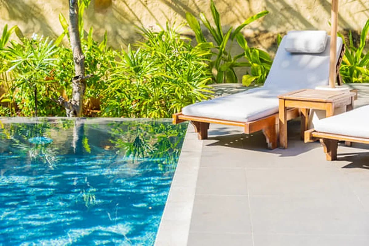 Lounge chairs beside a clear swimming pool with tropical plants