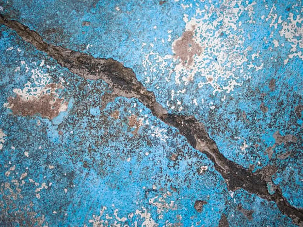 Cracked and peeling blue pool plaster with rust staining